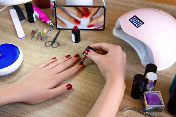 Girl paints her nails. Nail polish, mobile phone, ultraviolet lamp. Manicure at home. - Фото, зображення