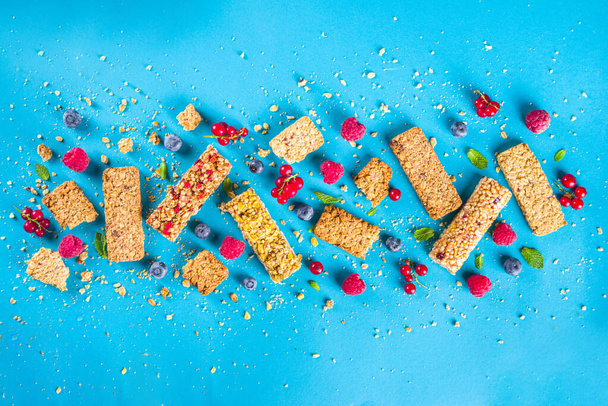 Concepto de snack saludable, barras de granola de cereales con bayas frescas y frutos secos en el espacio de copia de fondo azul - Foto, Imagen