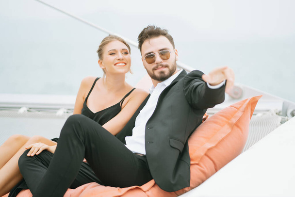 Mladý milující pár sedící na palubě plachetnice během plavby, dívající se daleko a ukazující k obzoru. Mladý pár si užívá den plavby. Romantika a dovolená - Fotografie, Obrázek
