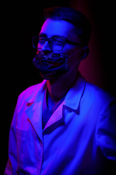 Young man doctor keeping face mask on blurred background. Medical mask on face. - Fotoğraf, Görsel