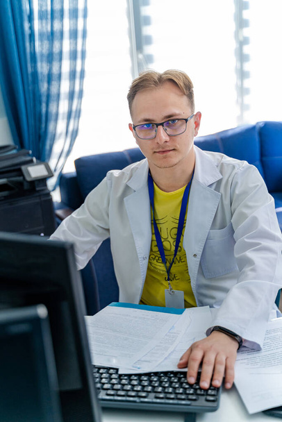 Serious doctor sitting at computer. Medical office. Doctor at work. Diagnosing. - 写真・画像