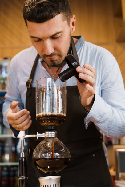 Barista sniffs flavored coffee in syphon device. Coffee brewing syphon alternative method. Advert for social networks for cafe and restaurant. - Photo, Image