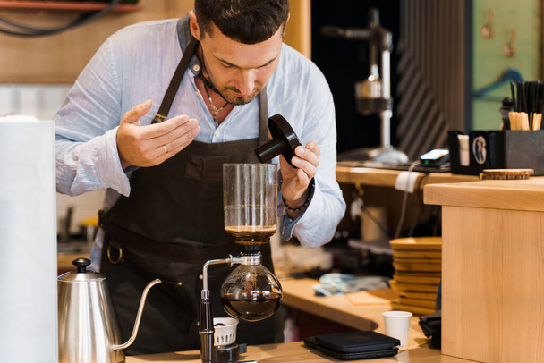 Barista sniffs flavored coffee in syphon device. Barista checks coffee in syphon. Coffee brewing syphon alternative method. Advert for social networks for cafe and restaurant. - Фото, изображение