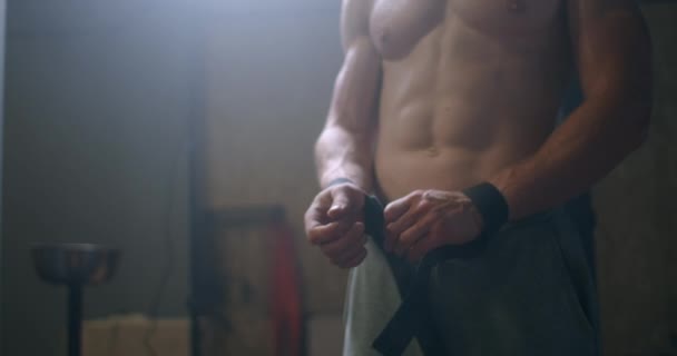 Young athletic Caucasian man changing, putting weight lifting straps on in gym locker room before workout slow motion. ties arms to barbell with fitness straps.  - Filmagem, Vídeo