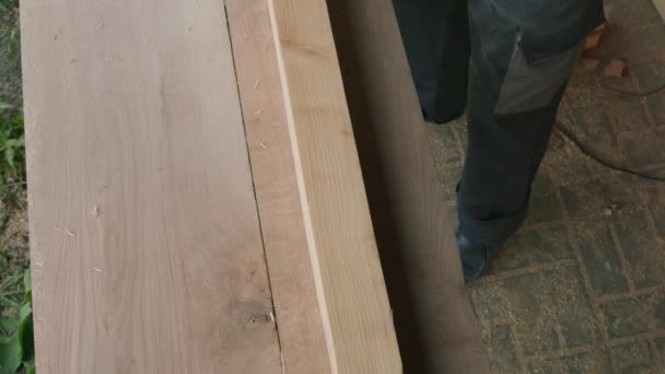 Samec tesař leští povrch dřevěné tyče s elektrickým hoblíkem v dílně. - Záběry, video