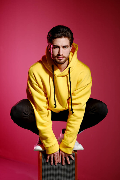 A young man of 25-30 years old in a yellow sweatshirt emotionally standing on an old music column on pink wall background.  - 写真・画像