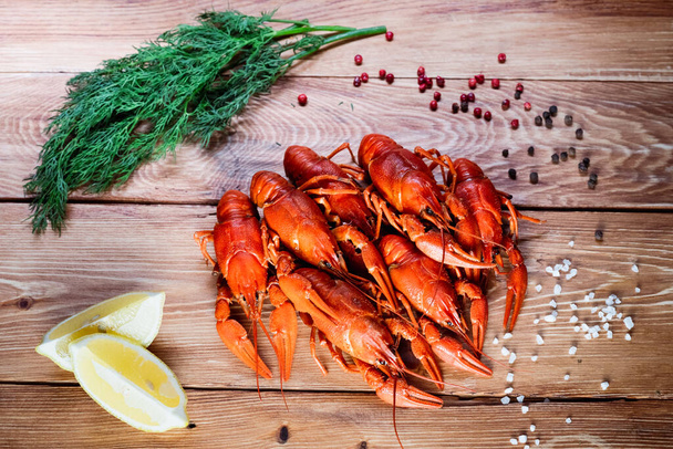 Boiled crayfish on a wooden table among spices, lemon and dill. The concept of food, beer snacks, relaxation in a bar and restaurant - Photo, image
