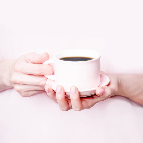 Vrouwelijke handen met roze kopje zwarte koffie op een lichtroze achtergrond. Kopieerruimte - Foto, afbeelding