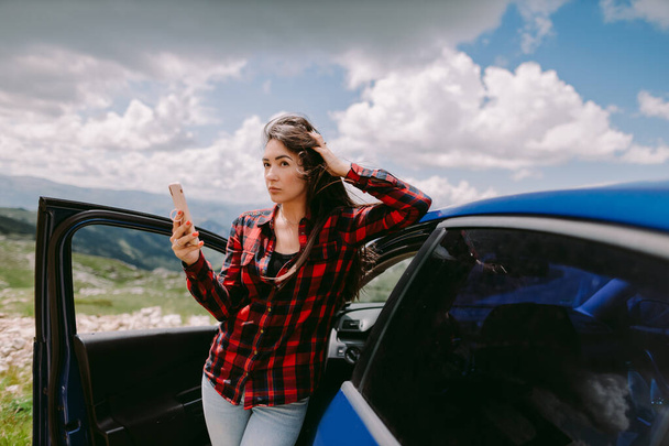 attractive woman travel by car and using smartphone in mountains - Photo, Image