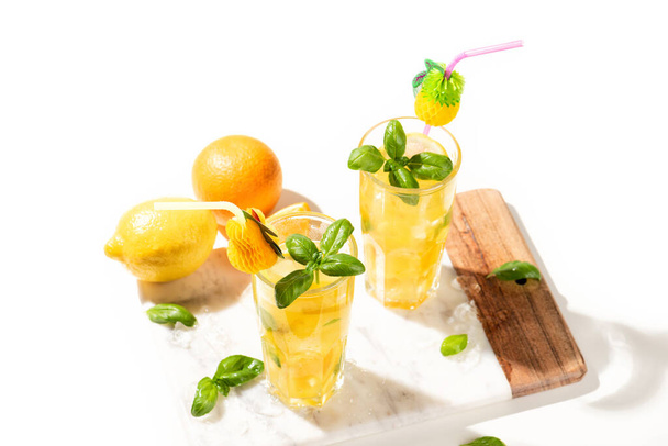 Цитрусовый лимонад или мохито коктейль с лимоном и апельсином и базиликом. Холодные напитки или напитки со льдом на мраморной доске - Фото, изображение