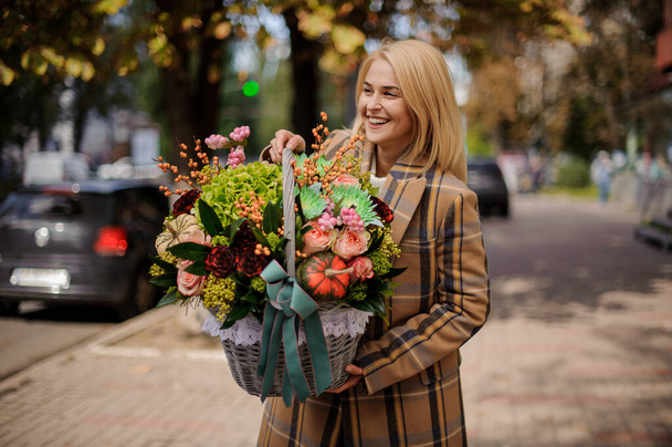 beautiful smiling woman in coat holds basket with flowers inside. - Fotoğraf, Görsel