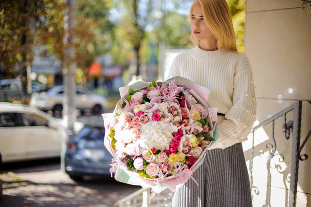 belle femme en pull blanc tient énorme bouquet de roses et regarde loin. - Photo, image