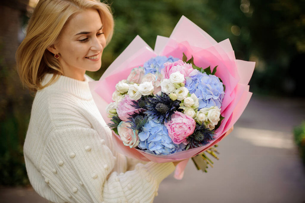 Cheerful woman holds bouquet of white, blue and pink flowers. - Zdjęcie, obraz