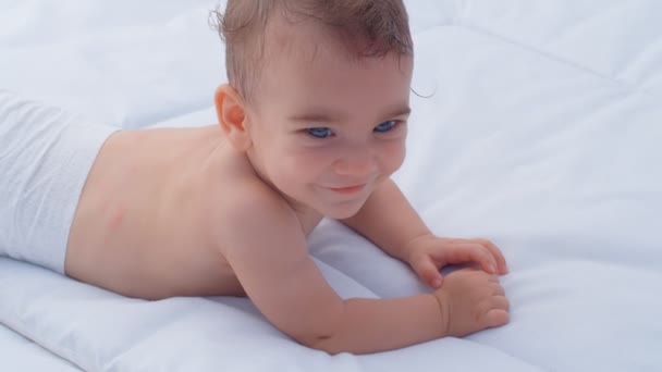Een kleine jongen van zes maanden kijkt om zich heen en lacht. Concept van de zorg voor kinderen en ouderlijke liefde, 4k slow motion - Video