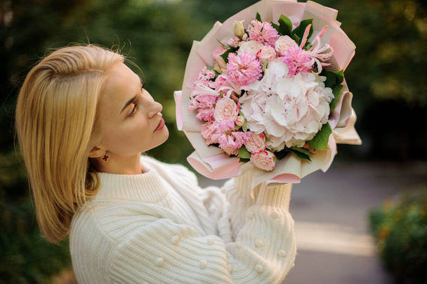 young woman holds delicate bouquet of pastel pink colors and looks at it - 写真・画像