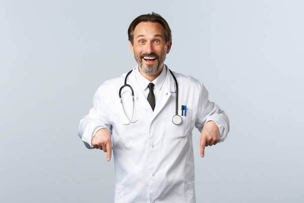 Covid-19, Coronavirus-Ausbruch, Gesundheitspersonal und Pandemiekonzept. Glücklich lächelnder Arzt in weißem Mantel, der zum Klicken einlädt. Therapeut zeigt Weg zur Werbung auf und lädt Patienten ein - Foto, Bild
