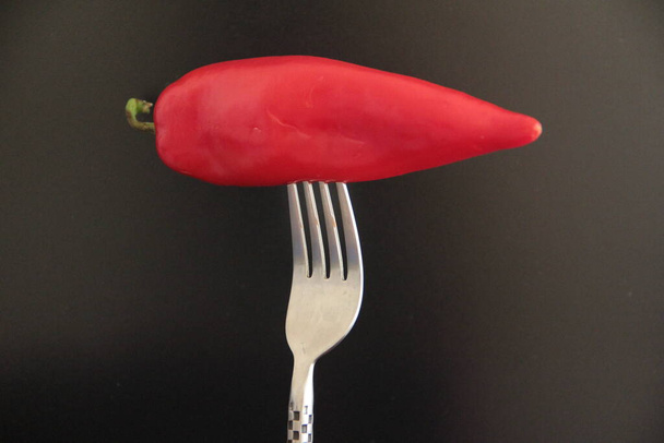 red pepper in the fork on a black background - Photo, Image