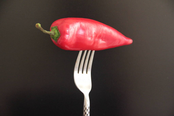 red pepper in the fork on a black background - Photo, Image