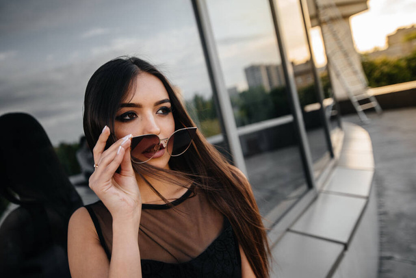 Stylish young and sexy girl posing in front of a business center in black. Fashion and style - 写真・画像