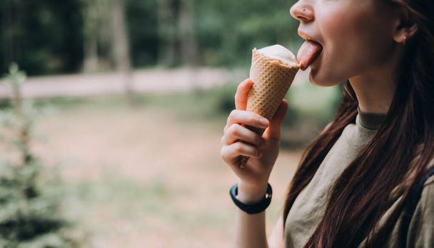 Young pretty woman eating ice cream in a waffle cone while walking along the street in the park alone. High quality photo - Фото, изображение