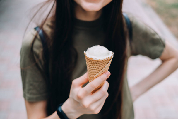 Young pretty woman eating ice cream in a waffle cone while walking along the street in the park alone. High quality photo - Φωτογραφία, εικόνα