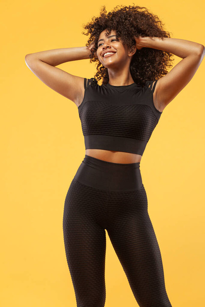 Lifestyle Concept. Portrait of beautiful happy and dancing African American woman with curly hair. Yellow studio background. Copy Space. - 写真・画像