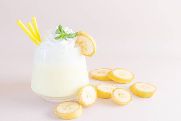 Milkshake de banana em um fundo leve em vidro transparente. Perto estão fatias de banana. O conceito de deliciosas bebidas frescas, comida saudável para o café da manhã e lanches
. - Foto, Imagem