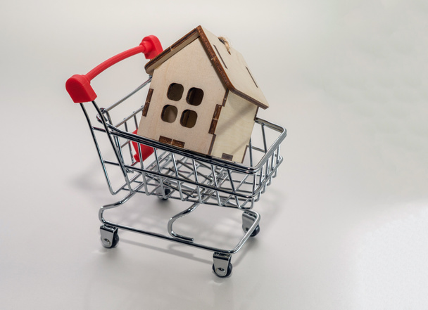El concepto de una hipoteca. Comprando bienes raíces. Un pequeño modelo de una casa de madera con un carrito de compras de juguetes
. - Foto, Imagen