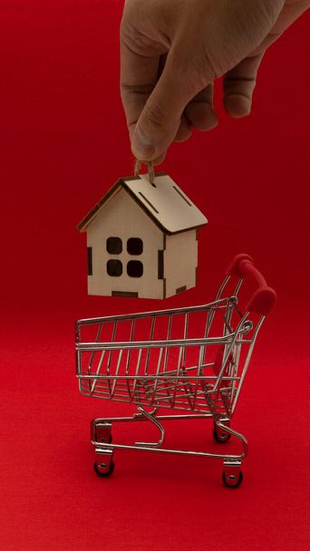 Ένδειξη ενυπόθηκων δανείων. Ψώνια για ένα σπίτι. Ένα μικρό μοντέλο ενός ξύλινου σπιτιού με ένα καλάθι αγορών παιχνιδιών. - Φωτογραφία, εικόνα