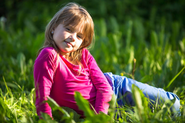 Egy tíz éves vicces lány fekszik a fűben.. - Fotó, kép
