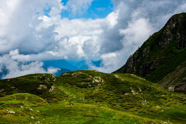 white clouds, blue sky, green pastures and spikes of granite rock in the Lagorai in the Trentino Alps near Lake Levico on a summer day - Photo, Image