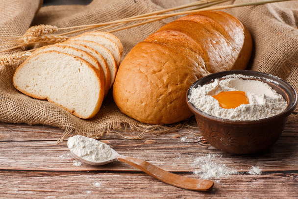 Close-up of homemade bread. Peasant loaf bread and wheat spikelets with space for text. Homemade baking. White bread with flour on wooden chopping board wheat - Photo, image