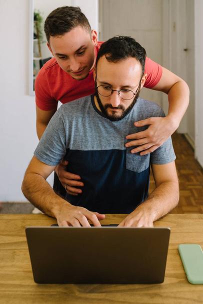 Stock photo of two caucasian adult men looking at a laptop thinking. One of them is standing holding a mug and has his arm on the others shoulder. - Foto, Imagen