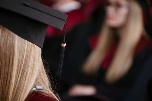 Jeune fille étudiante en attente pendant la cérémonie de remise des diplômes avec sa casquette de célébration en évidence et arrière-plan flou - Photo, image