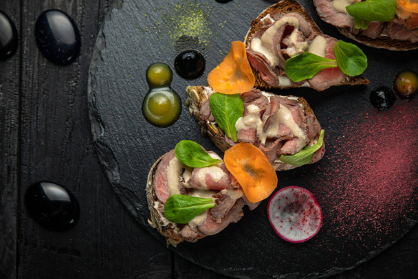 Meat bruschettas with cheese, vegetables, on a dark stone board - Foto, immagini