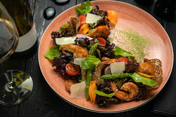 Salad with seafood, asparagus, tomatoes, sauce on a dark background - Fotó, kép