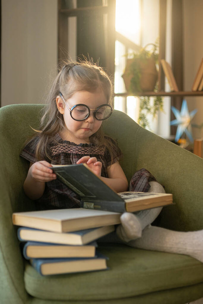 Little cute toddler girl in glasses reading books. back to school - Fotó, kép