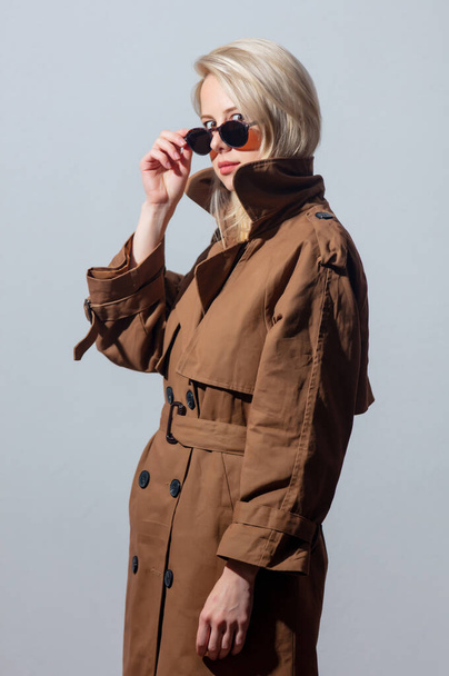 Blonde fille en lunettes de soleil et manteau sur fond gris  - Photo, image