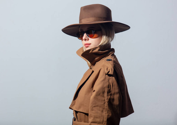 Stylowa kobieta w płaszczu, kapeluszu i okularach przeciwsłonecznych na szarym tle  - Zdjęcie, obraz