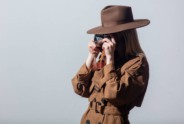 Жінка в капелюсі і плащі як шпигун з камерою на сірому фоні
.  - Фото, зображення