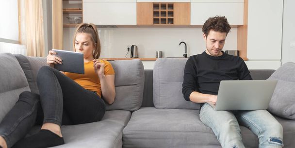 Crisis in a partnership, separation, internet addiction. Couple separated on sofa in living room - Φωτογραφία, εικόνα