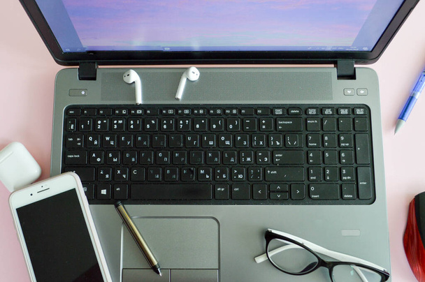 Lieu de travail à la maison, bureau à domicile pour le travail à distance avec un ordinateur portable téléphone portable téléphone portable stylo casque et lunettes sur un fond rose - Photo, image