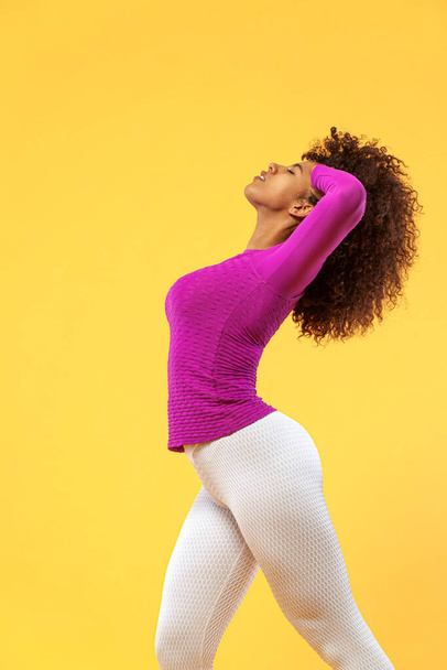 Smiling strong athletic woman with black skin and curly hair, doing exercise on yellow background wearing sportswear. Fitness and sport motivation. - 写真・画像
