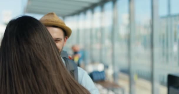 Нахабний молодий кавказький щасливий чоловік посміхається і зустрічає дівчину або дружину з далекої подорожі на автобусній зупинці. Повертаюся додому з подорожі. Пара закоханих зустрічає увагу туристів, які обіймають хлопця - Кадри, відео