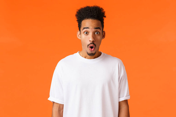Surprises, amazement concept. Astonished and impressed handsome young college student, african-american guy, folding lips staring amazed, gasping wondered say wow, standing orange background - Photo, Image
