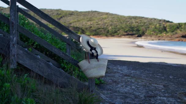 Pohled na písečnou pláž se slaměným kloboukem a taškou zavěšenou na dřevěných schodech. - Záběry, video