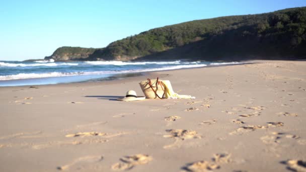 わら帽子、バッグ、ショール付きの日当たりの良い海のビーチ。青い波が砂を打つ. - 映像、動画