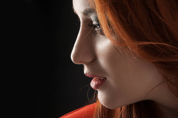 Dramatic portrait in side profile silhouette of woman posing with hard shadows in studio, sexy shot. Caucasian person, black top shirt, long redhead ginger hair isolated on black studio background - Photo, image