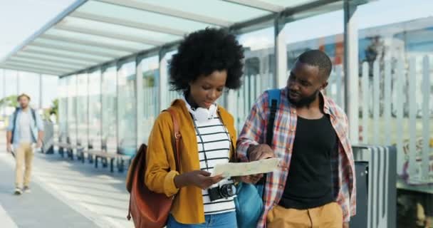 Afrikai-amerikai fiatal turisták sétálnak a szabadban térképpel és keresik a megfelelő útvonalat. Gyönyörű nő és jóképű férfi utazók beszélnek és megvitatják, hogyan válasszanak a várostervezés. - Felvétel, videó