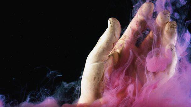 Primer plano de una nube de tintas rosadas brillantes que se extiende bajo el agua alrededor de la mano artificial. Imágenes de archivo. Figura de mano y pinturas aisladas sobre fondo negro
. - Foto, Imagen